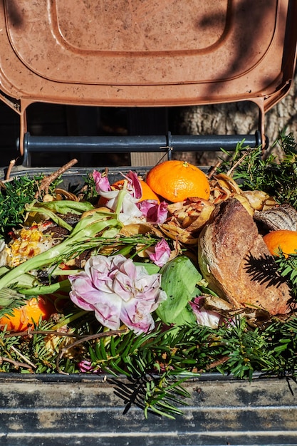A close-up shot of a compost bin in a garden, filled with organic waste such as fruit peels, vegetable scraps, and coffee grounds. The compost is dark and rich, illustrating the process of decomposition.