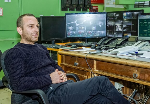 A security analyst working at a computer, monitoring network traffic and system logs for signs of intrusion. The image is focused on the analyst's serious expression and the complex data displayed on the screen.