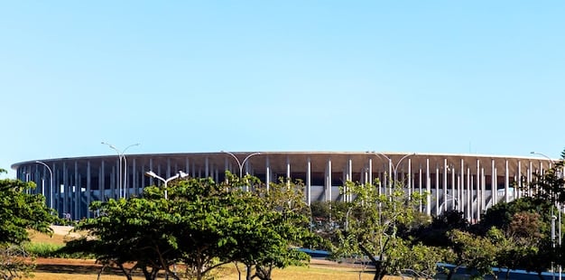 A modern factory with solar panels on its roof, a clear exhaust pipe, and lush greenery around its perimeter, symbolizing environmentally conscious industry.