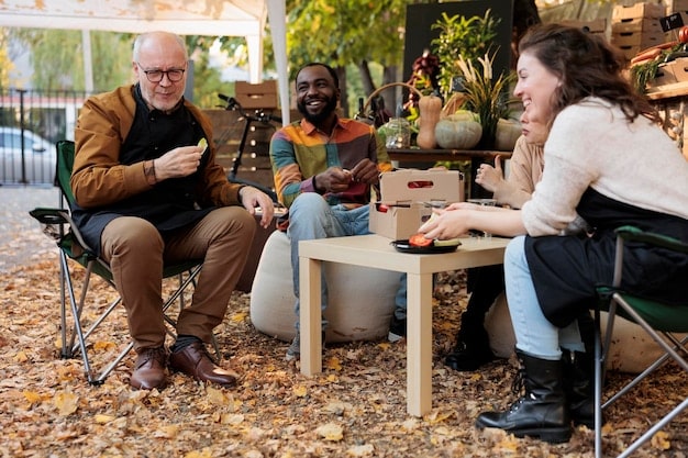 A community gathering, possibly a workshop or storytelling session, where people of different ages are listening to an elder who is sharing traditional knowledge about local plants and animals. The setting is natural and inviting.