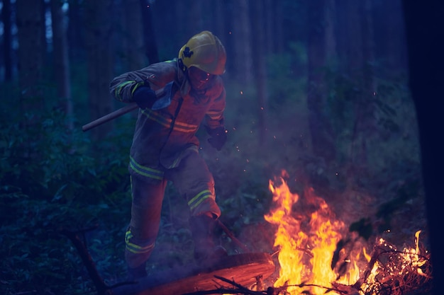 Firefighters battling a large forest fire at night, illuminated by the flames and searchlights, with thick smoke obscuring the background.