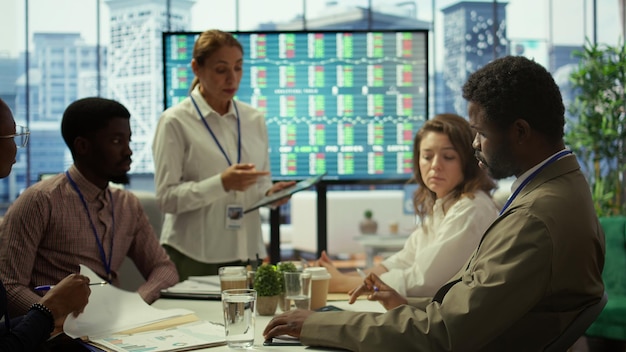 A diverse group of business professionals in a boardroom engaged in a serious discussion, reviewing charts and economic forecasts on a large screen.